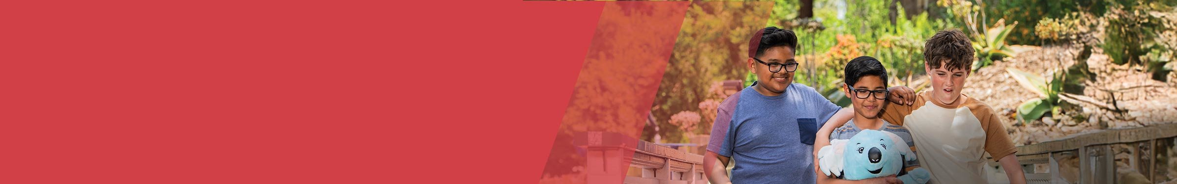 Red section header with three boys to the right walking together outdoors with arms around each other. The boy in the center holds a blue stuffed koala. All appear happy and relaxed in a sunny, landscaped setting.