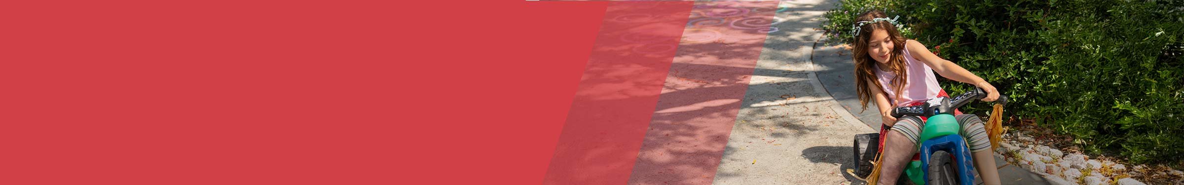 Red section header with young girl to the right with overgrowth on leg riding a colorful tricycle on a sunny path, wearing a flower crown and smiling as she turns the handlebars.