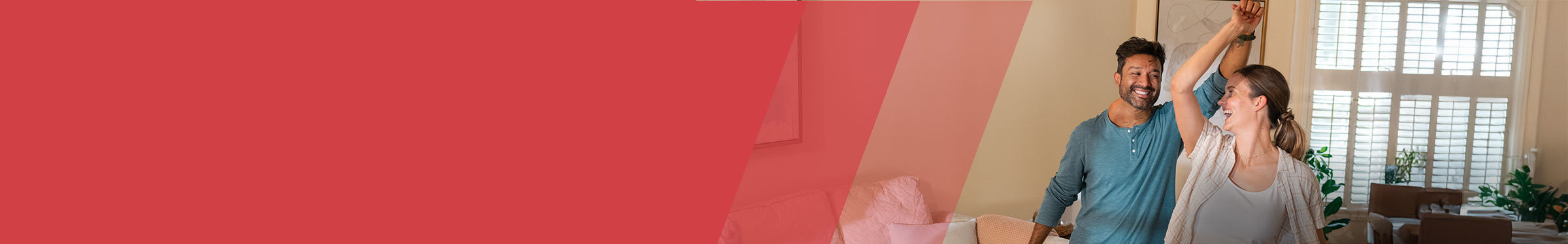 Red section header with a smiling man and woman dancing together in a bright, sunlit living room. The man in a teal shirt lifts the woman’s arm as she spins, both appearing joyful and relaxed. The background features tall windows with white shutters and indoor plants.